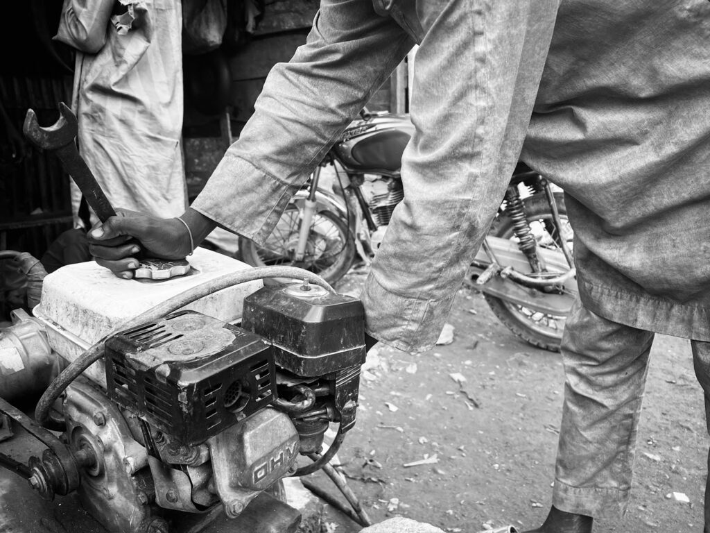 A mechanic's hands fixing an engine with tools, in a black and white photo.