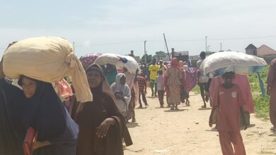 People carrying large sacks on their heads walking down a busy street.