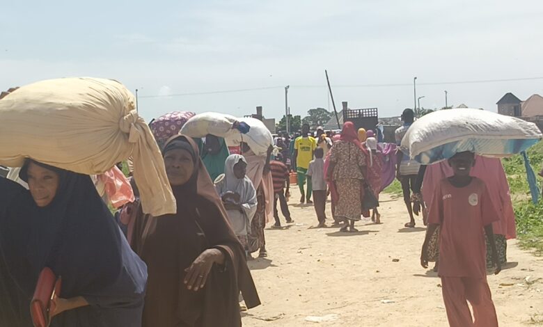 People carrying large sacks on their heads walking down a busy street.