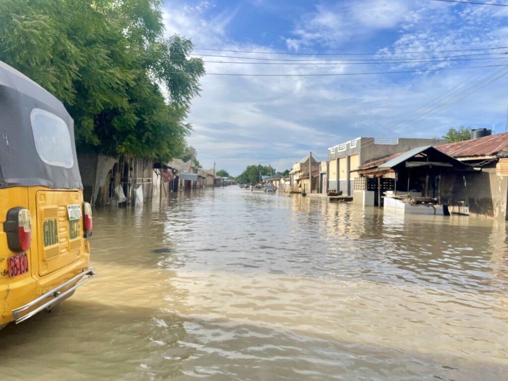 Flooded street with submerged shops and a partially visible yellow auto-rickshaw on the left.