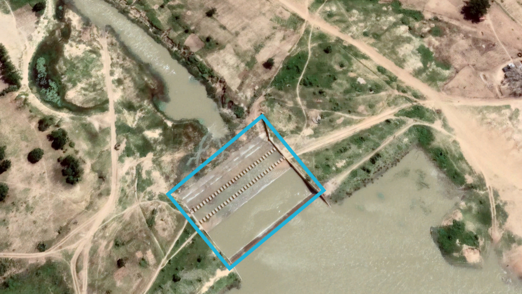 Aerial view of an aquaculture farm near a river, with rectangular ponds and access paths.