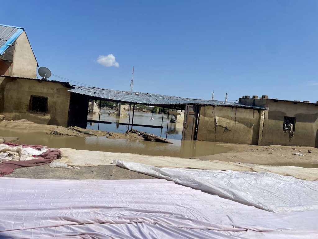 Flooded area with submerged houses and fabrics laid out to dry in the foreground under a clear sky.