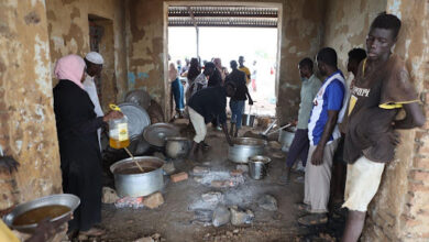 People preparing food in a rustic kitchen with basic utensils and open fire.