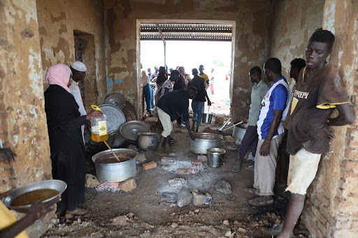 People preparing food in a rustic kitchen with basic utensils and open fire.