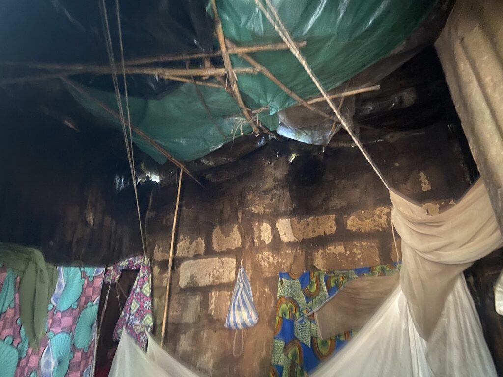 Interior of a makeshift shelter with tarp ceiling, draped fabrics, and rough walls.