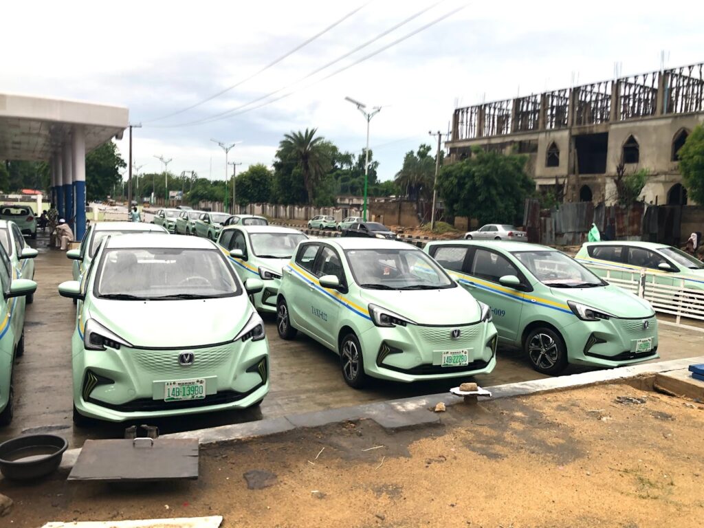 A fleet of mint-green and blue taxis lined up at a charging station.