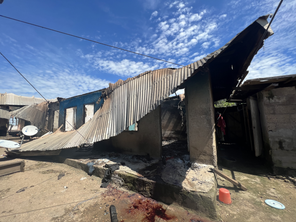 Dilapidated structures with corrugated metal roofs under a blue sky with scattered clouds.