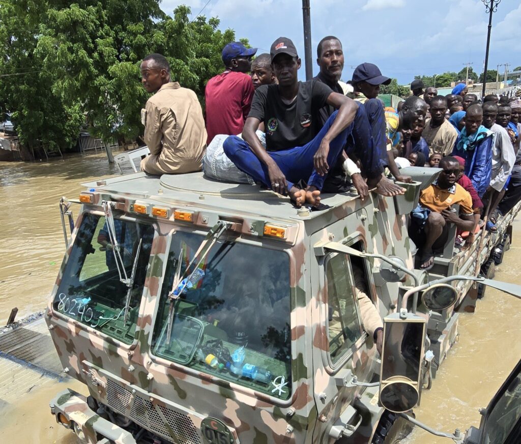 People sitting on a military vehicle in a flooded area.