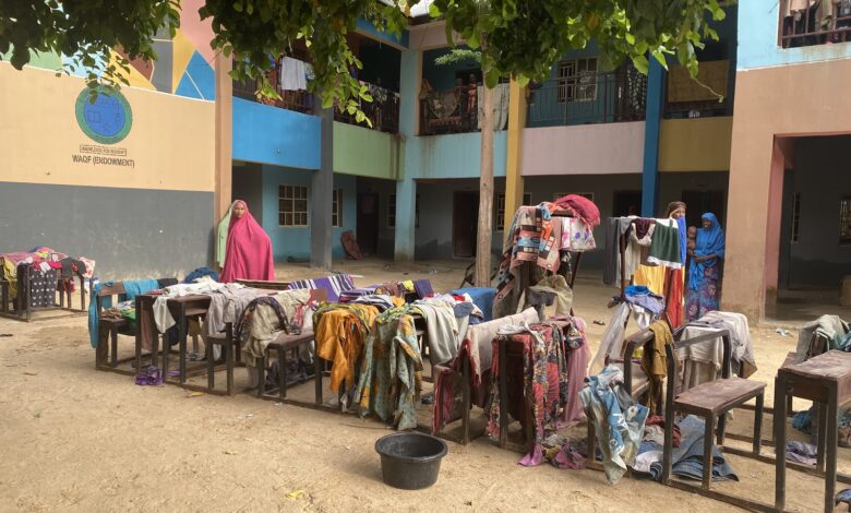 Colorful clothing laid out on tables and benches to dry in a sunlit courtyard, with women standing nearby.