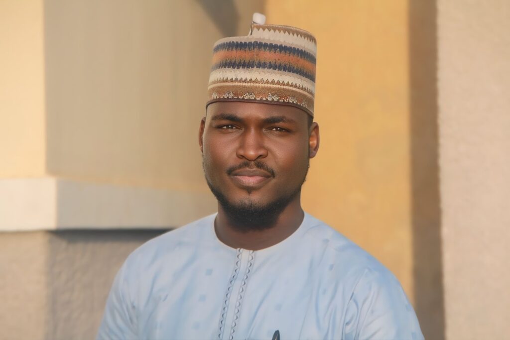 A man in traditional attire with a patterned cap, looking at the camera against a soft background.