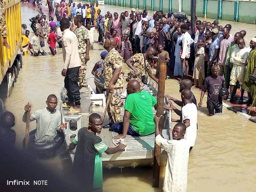 People navigating through flooded streets with makeshift rafts and aid from military personnel.