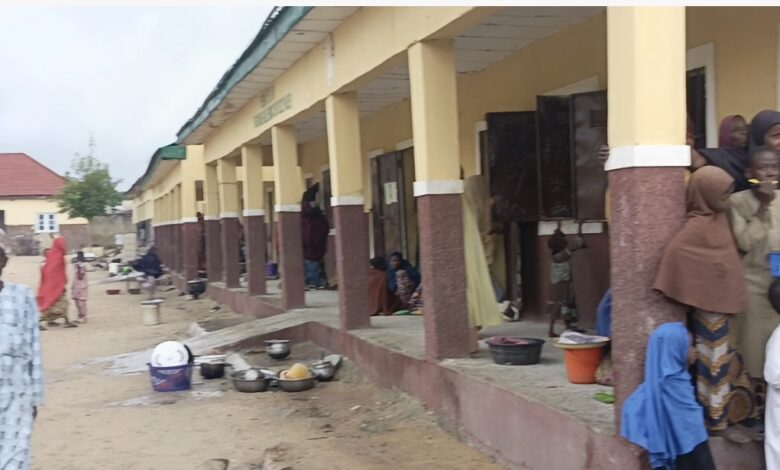 People outside a building with columns, some sitting, with pots and utensils around.