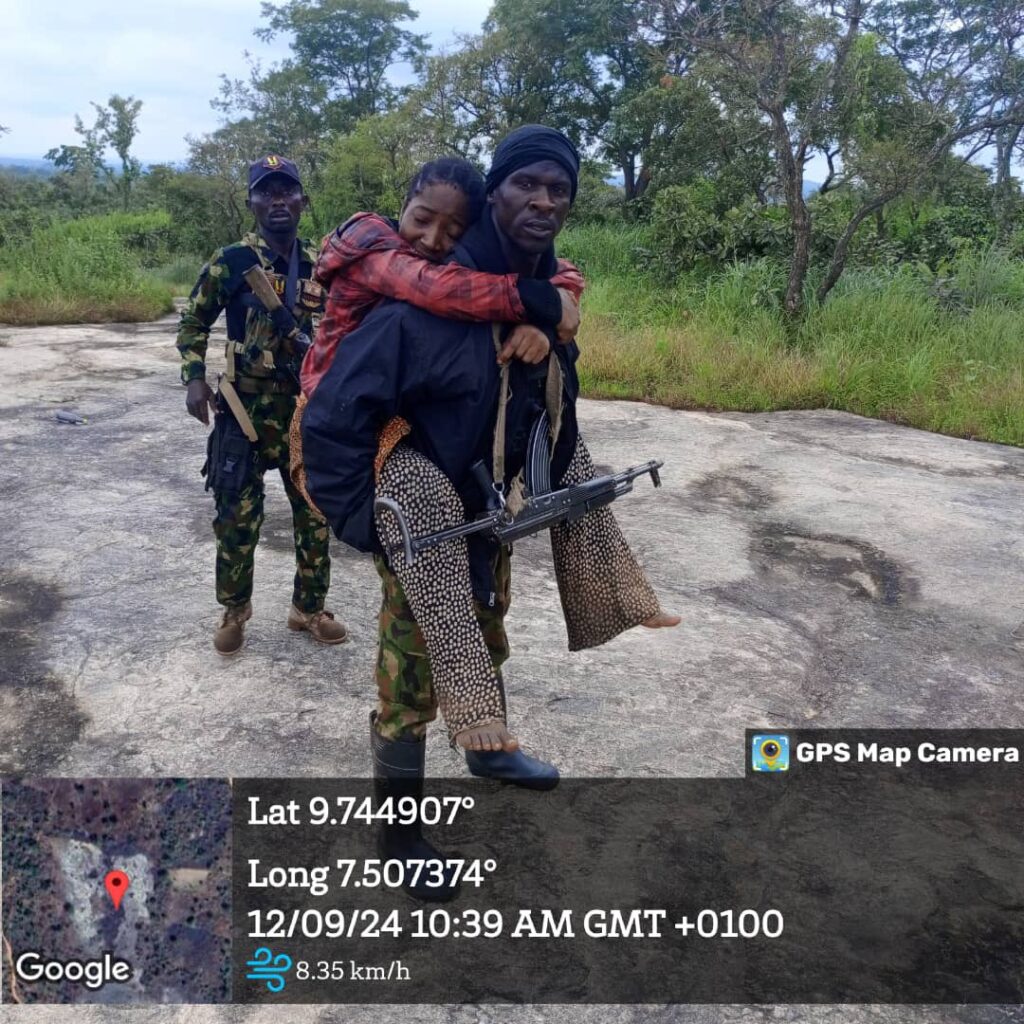 Two armed men in camouflage, one carrying another person, in a natural outdoor setting with GPS data overlay.