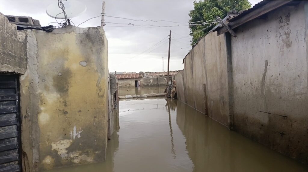 Flooded urban area with water between deteriorating walls and buildings, under an overcast sky.