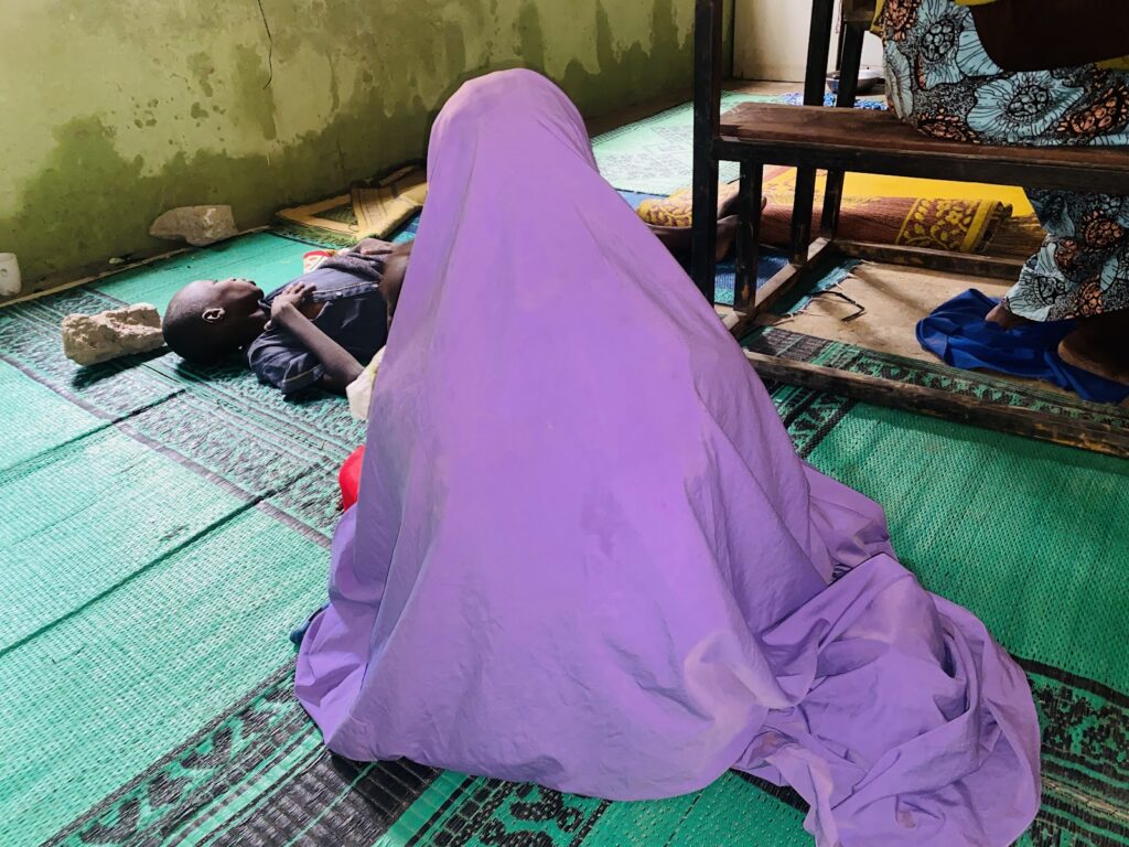 Person lying under a purple mosquito net in a room with green mat flooring.