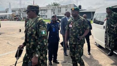 Military personnel walking on a tarmac with a white van and building in the background.