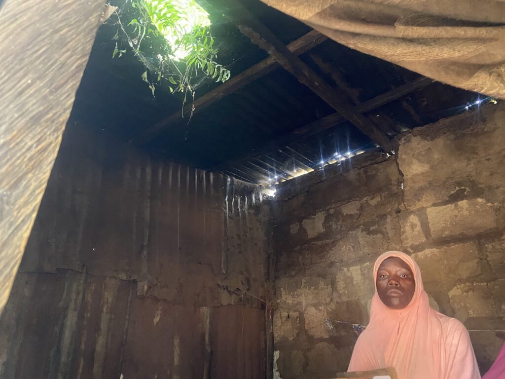 Person in a pink garment inside a dimly-lit room with sunlight peeking through roof holes.