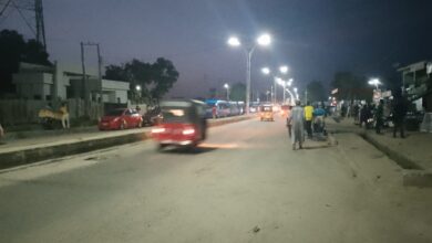 A busy street at twilight with pedestrians, vehicles, and street lighting.