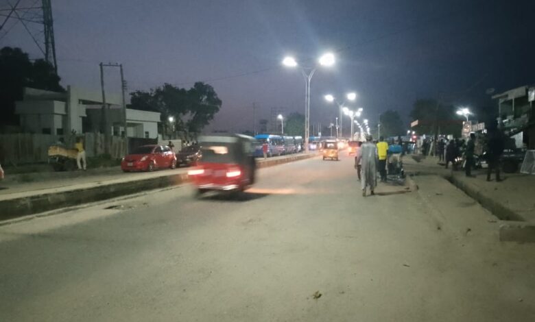 A busy street at twilight with pedestrians, vehicles, and street lighting.