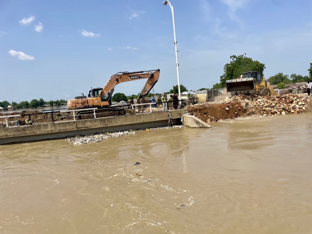 Construction machinery working on a riverside with a partially submerged barrier.