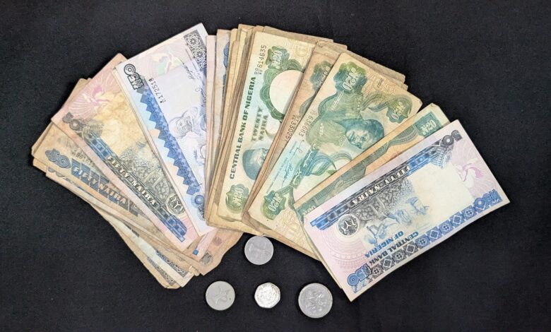 Assorted Nigerian naira banknotes and coins spread out on a dark surface.