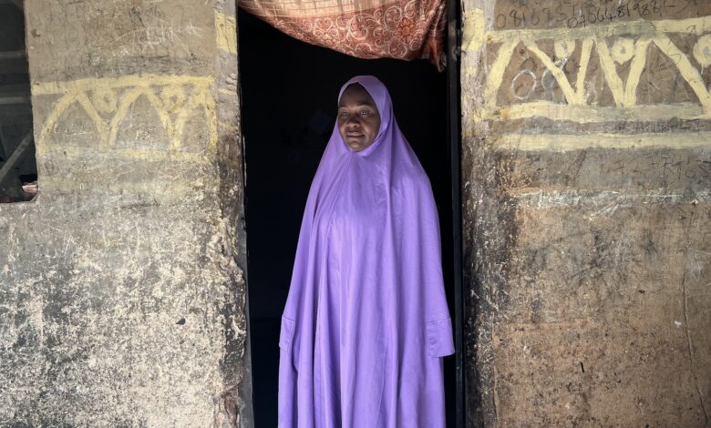 Woman in purple attire standing in a doorway with graffiti on the wall.