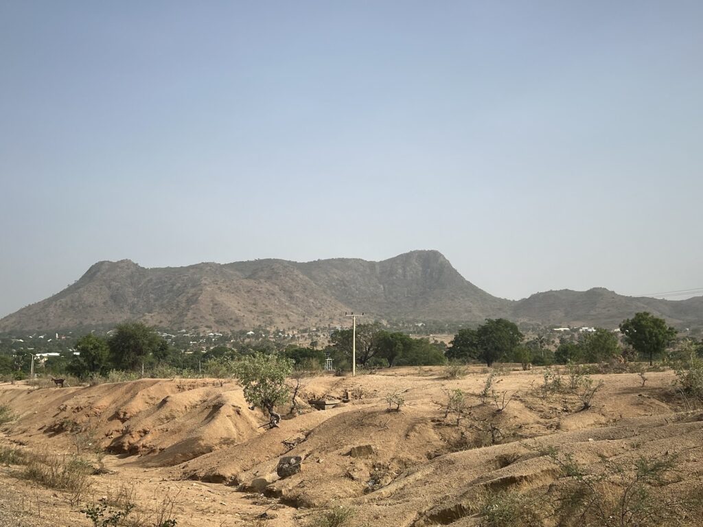 Arid landscape with rocky hills in the background and sparse vegetation in the foreground under a clear sky.