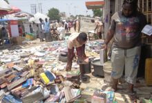 Street book market with people browsing piles of books on the ground under the sun.