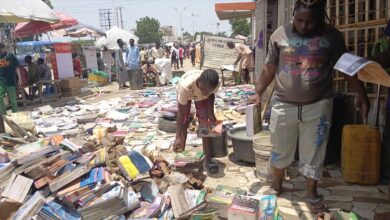 Street book market with people browsing piles of books on the ground under the sun.