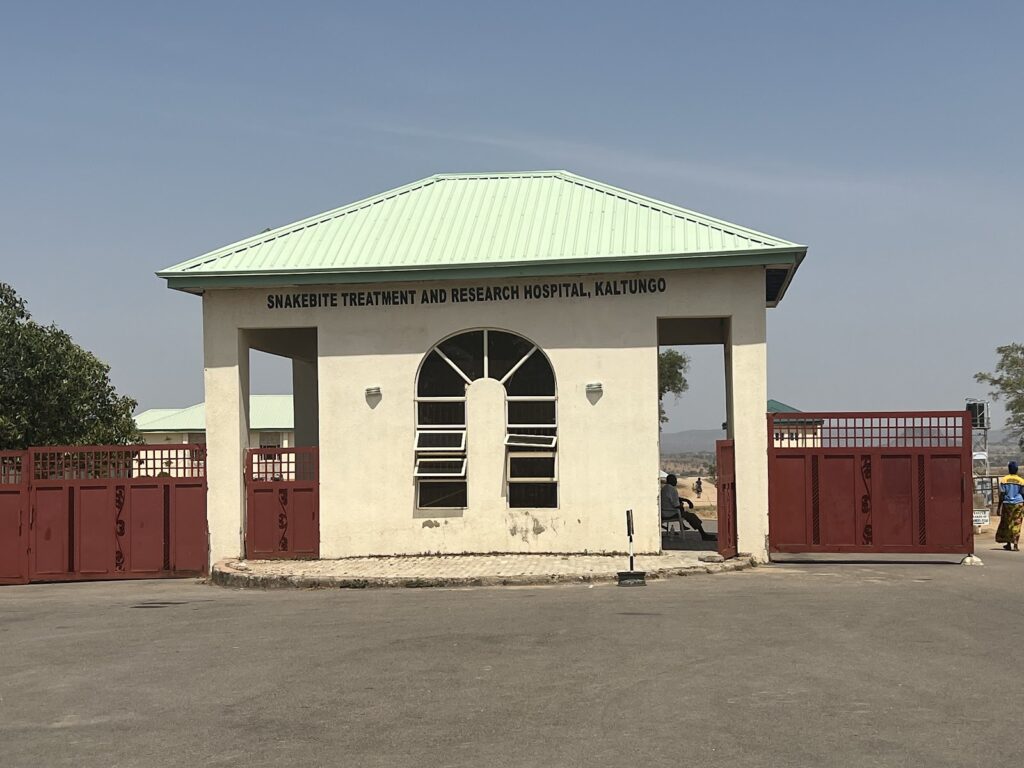 Front view of Snakebite Treatment and Research Hospital Kaltungo with red gates and a clear sky.