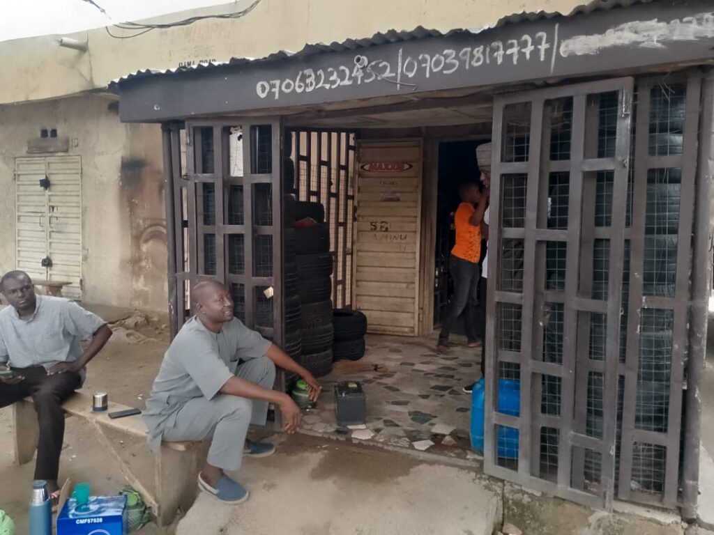 Two men sitting outside a tire repair shop with phone numbers painted above the entrance.