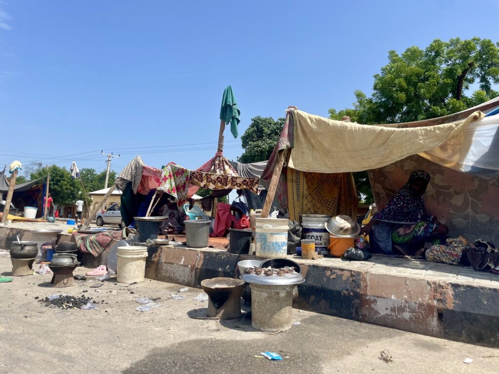 Street vendors under makeshift canopies with cooking pots and utensils in an outdoor market.