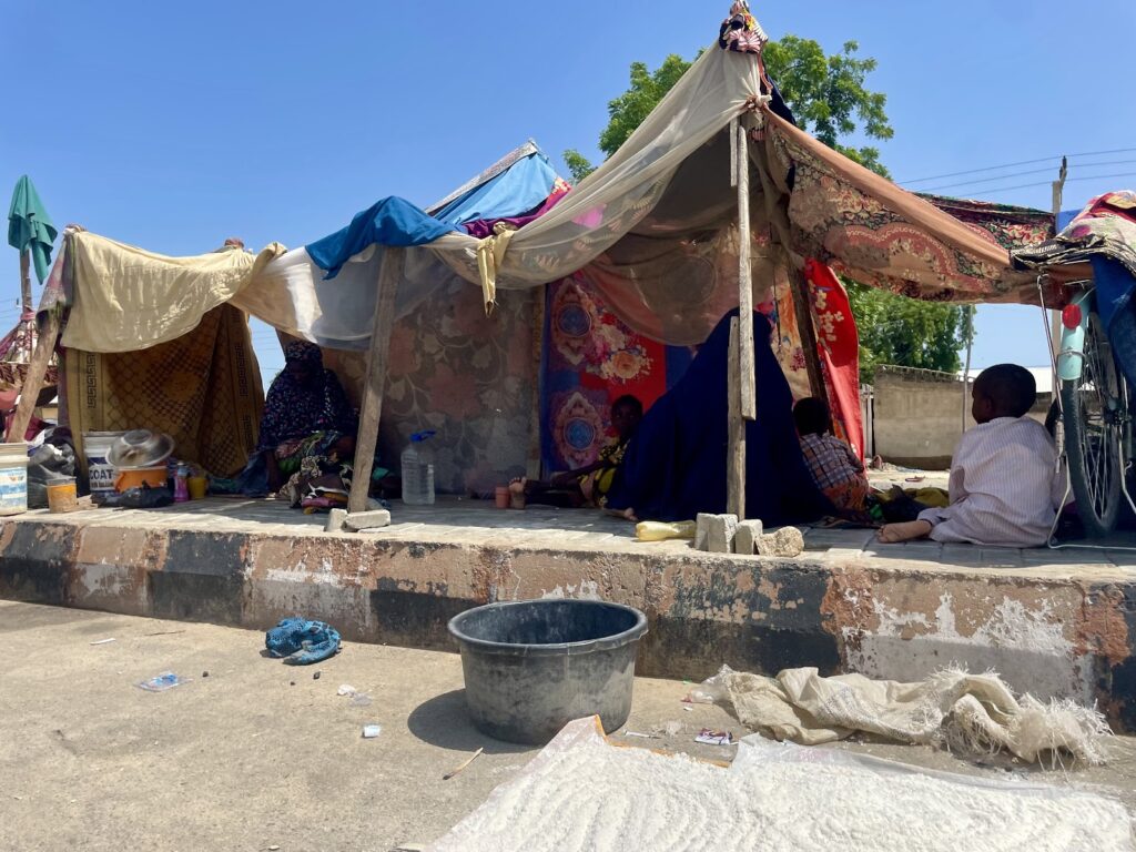 Informal tent shelter with people sitting inside on a sunny day.