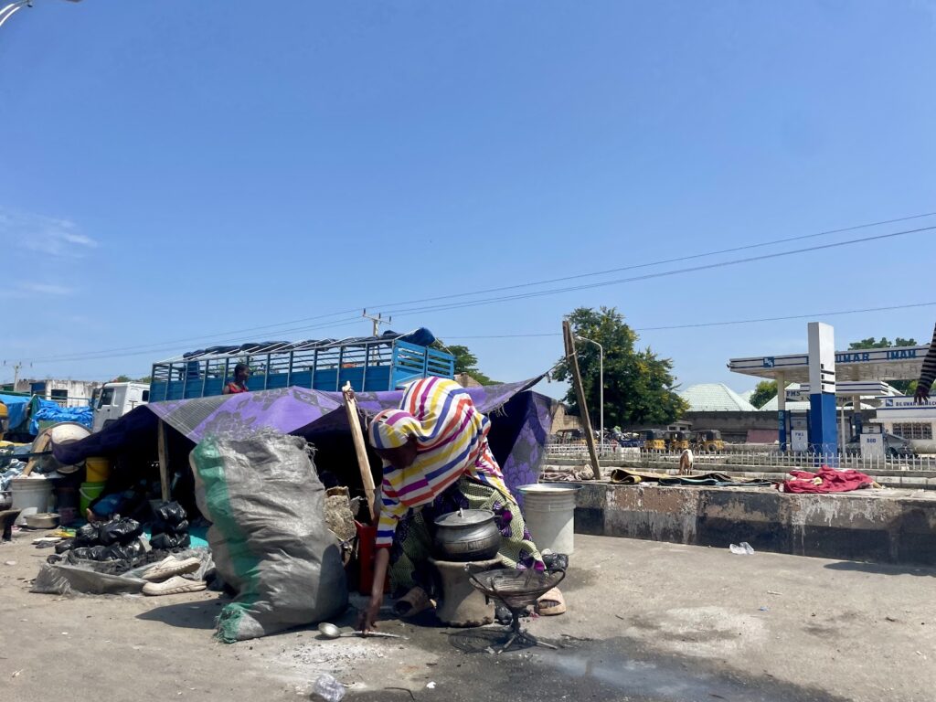 A person arranging items under a makeshift shelter on a sunny day amidst urban surroundings.