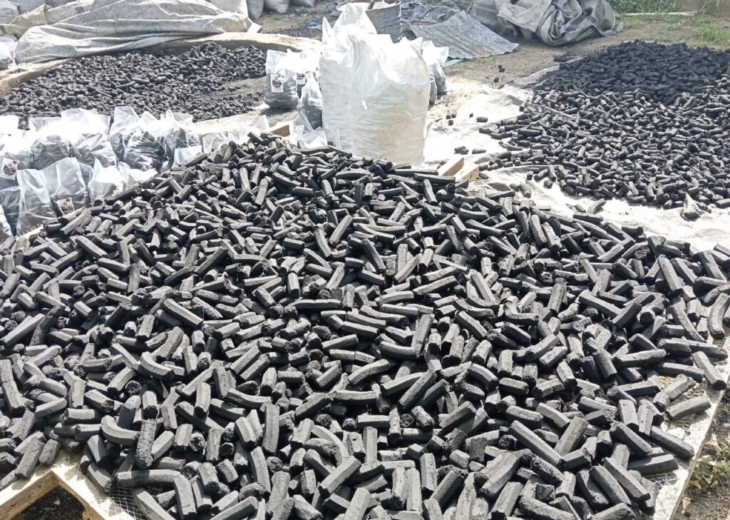 Piles of charcoal briquettes drying outdoors with some packed in sacks.