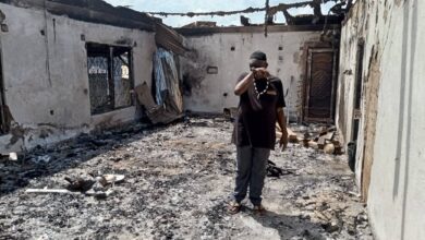 Man standing amidst the ruins of a burnt building, covering his nose.