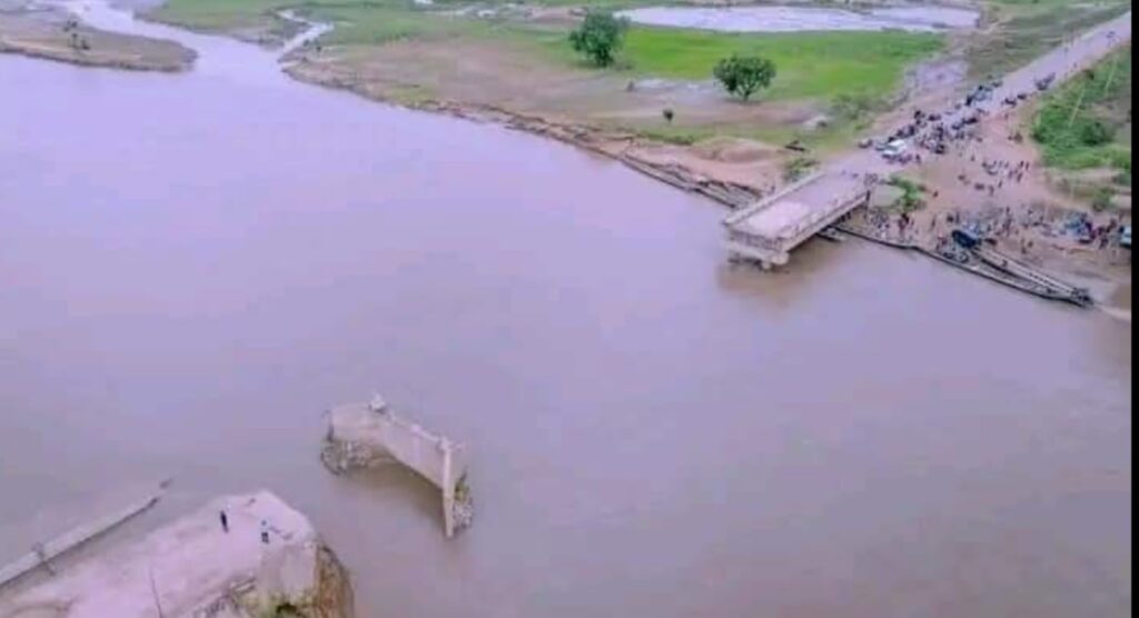 Aerial view of a collapsed bridge over a river with people gathering near the site.