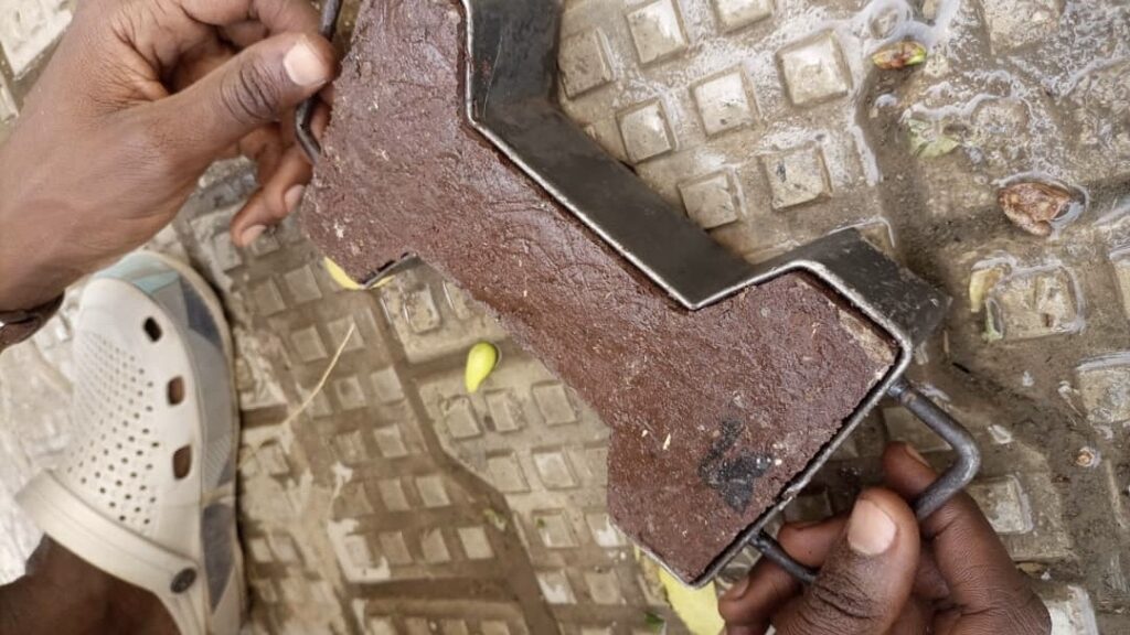 Hands holding a rusty metal object against a patterned ground with a white shoe partially visible.