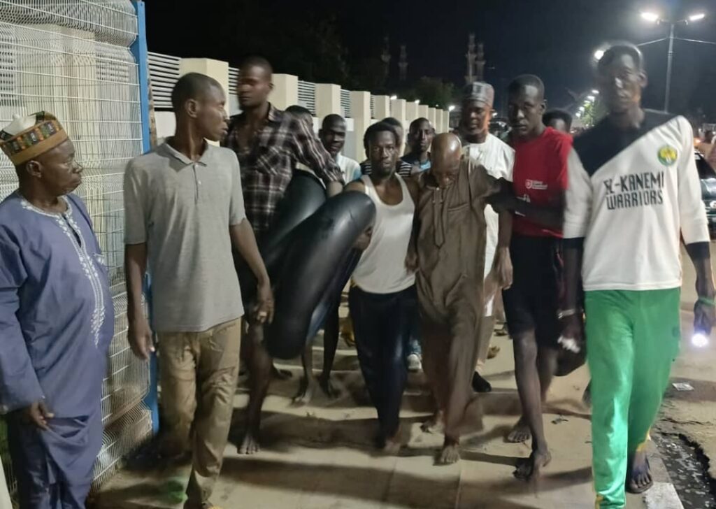 A group of men walking at night, one carrying a large object, possibly in a lively discussion or activity.