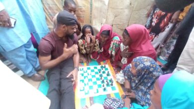 Group of people gathered around a chessboard, engaged in a game and conversation.