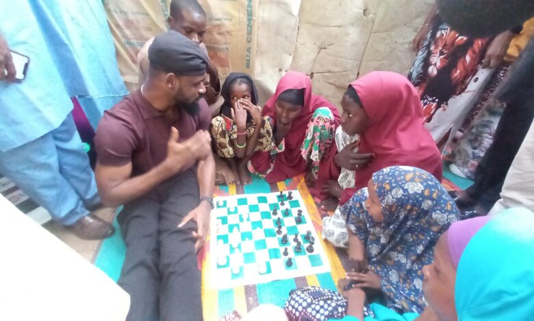 Group of people gathered around a chessboard, engaged in a game and conversation.