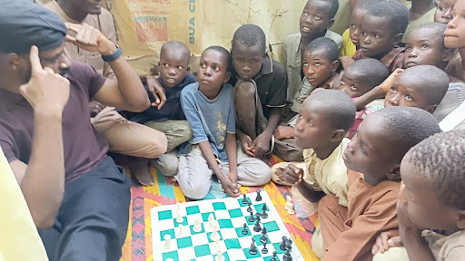 Group of children sitting around a chessboard with an instructor, eagerly learning how to play.