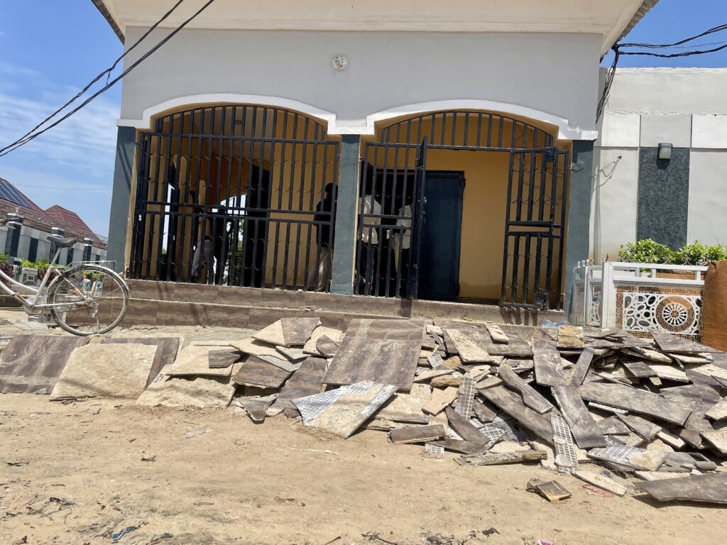 A house with a gated entrance and scattered construction debris in the foreground.