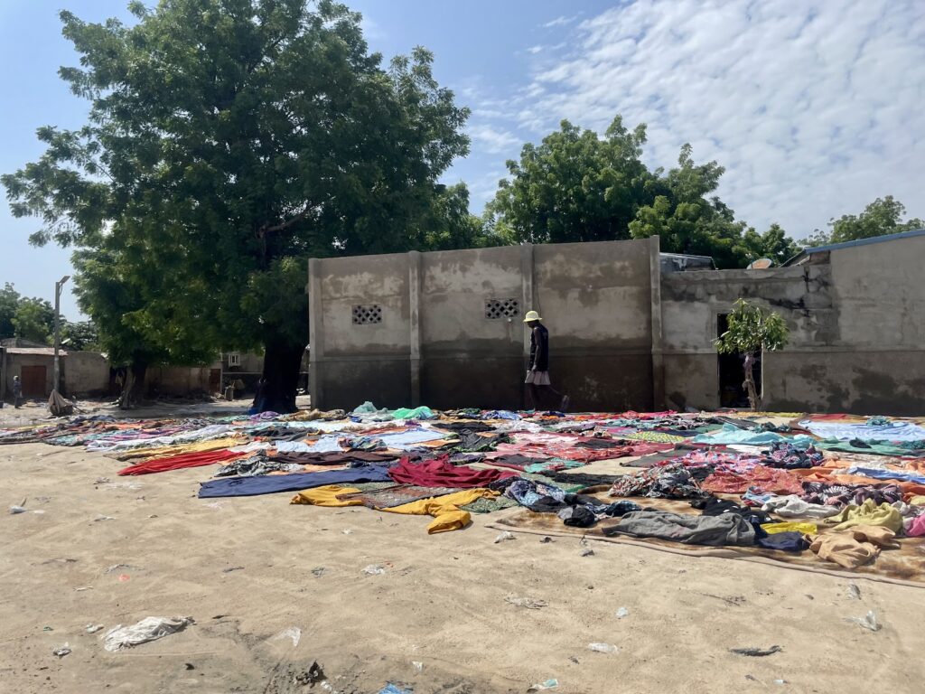 Clothes spread out on the ground to dry with trees and a wall in the background, person walking beside the wall.