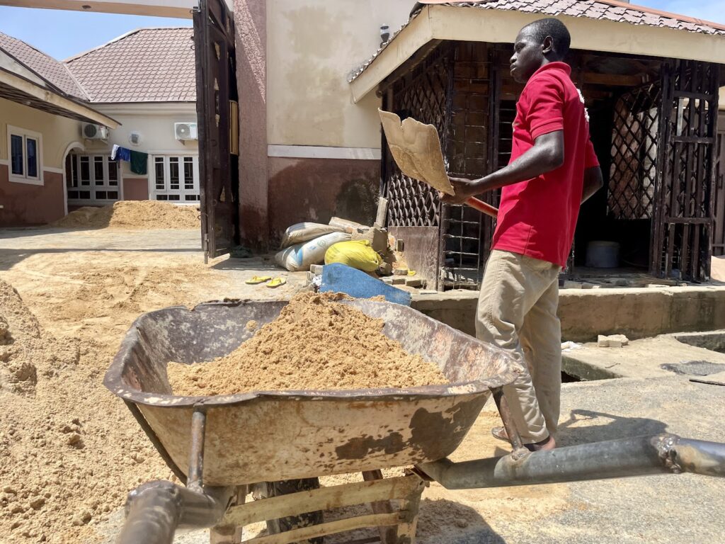 Man shoveling sand into a wheelbarrow at a construction site on a sunny day.