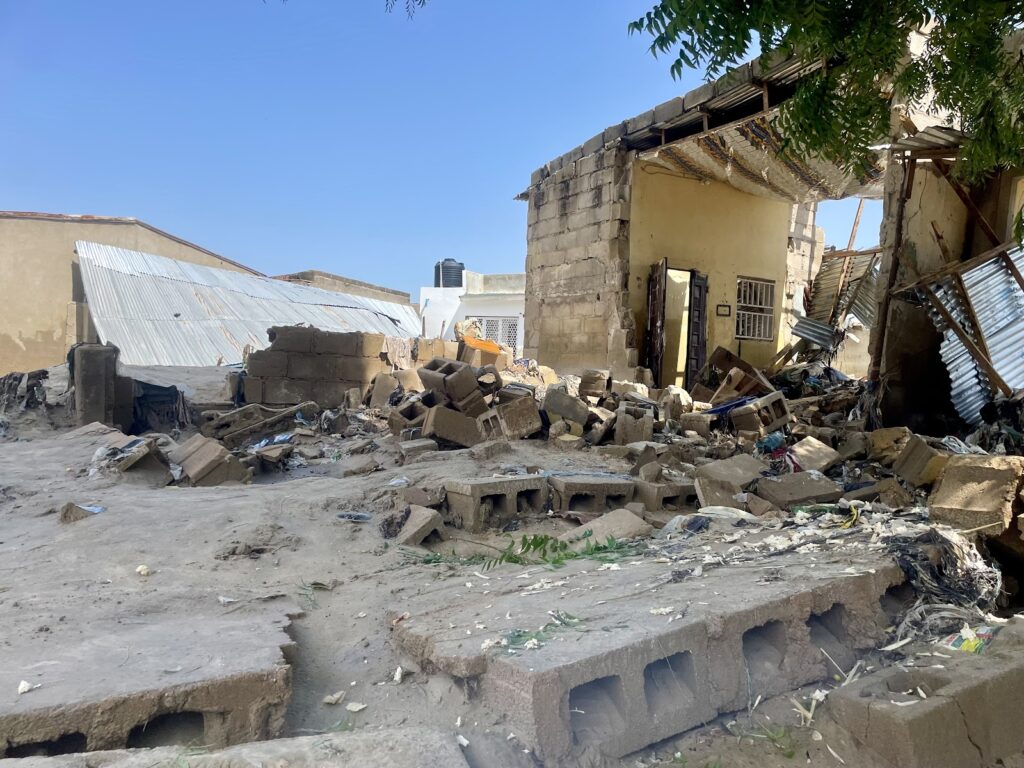 Rubble from a collapsed building with blocks strewn across the ground under a sunny sky.