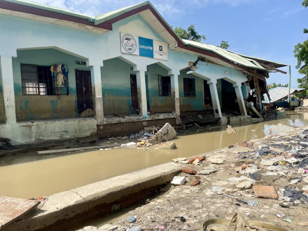 A damaged building with UNICEF sign, partially submerged in water with debris around.