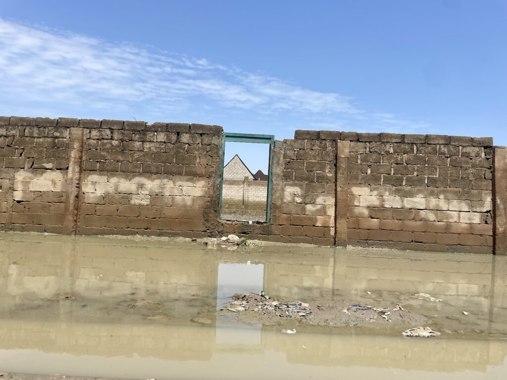 A dilapidated brick wall with a doorway framing a distant pyramid, standing water in the foreground.