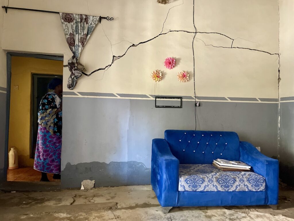 A woman walking through a doorway in a room with a cracked wall and a blue sofa with magazines.