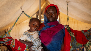 Woman in colorful shawl carrying a child on her back inside a tent.